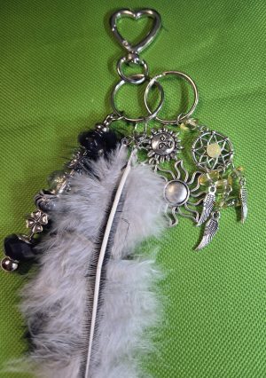 Handmade celestial bag charm with black-and-white feathers, silver-tone sun charms, miniature dreamcatcher, decorative beads, and heart-shaped clasp.