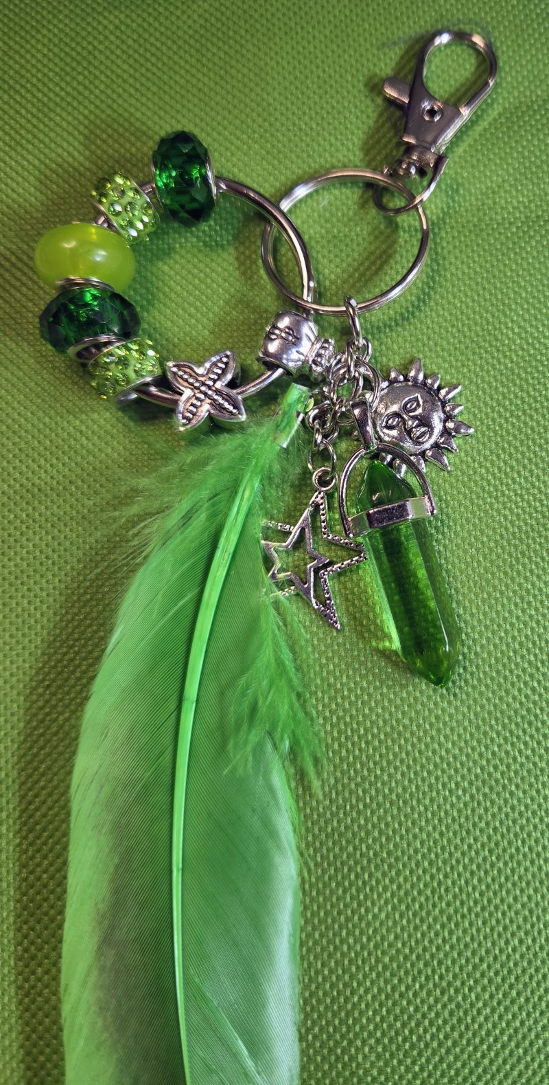 Handmade green feather bag charm with emerald and lime-green beads, silver-tone sun and star charms, green crystal-style pendant, keyring and lobster clasp.