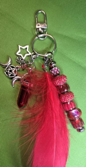 Handmade red feather bag charm with sparkling red beads, silver moon and star charms, pentacle accents, and red crystal-style pendant.